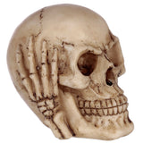 Angled close-up view of a beige skull ornament, with its left hand covering the eye sockets, depicting the 'See No Evil' motif.