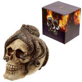 Angled view of a beige skull ornament with textured bronze octopus tentacles wrapped around it, presented alongside its purple and orange display box.