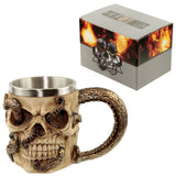 Angled view of a decorative bone-coloured skull tankard, featuring bronze-effect octopus tentacles entwined around it and forming the handle, with a metal inner lining. Its grey packaging box, adorned with orange flame-like designs, is partially visible in the background.