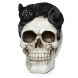 Front view of a Skull with Black Cat Ornament figurine, featuring an aged, off-white skull with dark eye sockets and detailed teeth, and a black cat with green eyes lying on top.