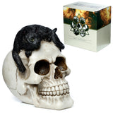 Detailed view of a cream skull ornament with a black cat featuring vibrant green eyes and textured fur curled on its crown, presented on a white background alongside its patterned packaging box.