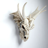 Angled view of an ivory-coloured dragon skull decoration, featuring prominent horns, textured wing-like elements, and intricate silver-coloured metallic detailing, on a white background.