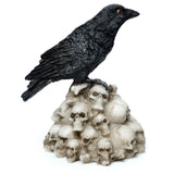Angled view of a black crow figurine with red eyes and textured feathers, standing on a pile of light-coloured skull ornaments.