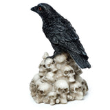 Angled view of a black crow ornament with textured feathers and red eyes, standing on a pile of weathered off-white skull figurines.