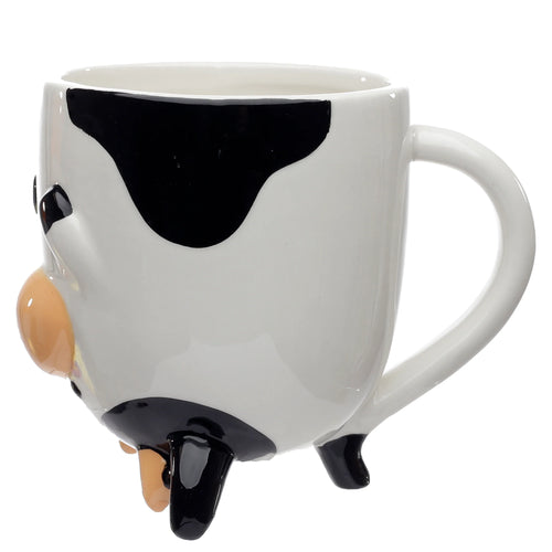 Angled view of a white ceramic upside down mug, shaped like a cow, with black patches, a beige snout, black hooves, and beige udders, on a white background.