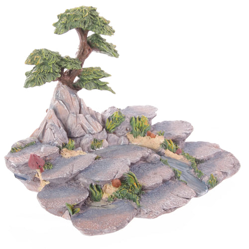 Angled view of a Flower Fairy World figures display stand, depicting a detailed miniature rocky landscape with a large tree, winding blue stream, and green foliage with red mushrooms.