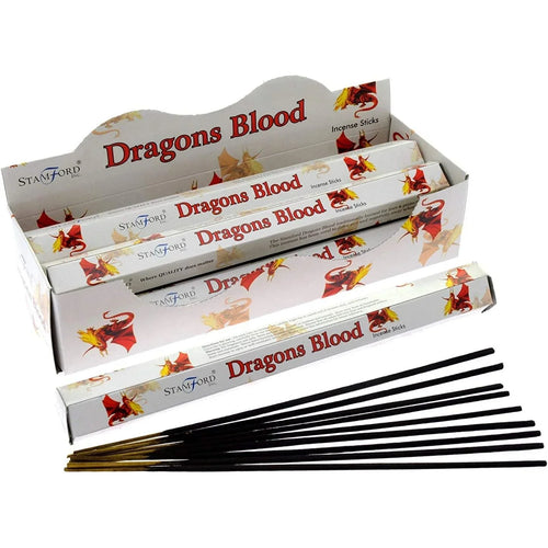 Angled view of a white display box for 'Dragons Blood' incense sticks, featuring red and yellow dragon illustrations. The box contains several packaged incense sticks, with a pile of loose black incense sticks lying in front, all on a white background.