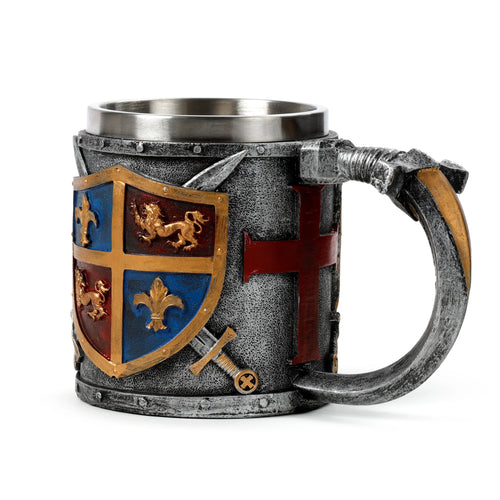 Front angled view of a decorative tankard, showcasing a gold and silver coat of arms shield with blue and red quadrants featuring gold fleur-de-lis and lion heraldry. The main body of the tankard is textured grey with a red cross motif and silver sword and dagger embellishments. The handle also features textured silver and gold detailing.