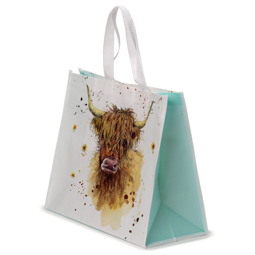 Angled view of a reusable shopping bag featuring a Jan Pashley Highland Coo cow illustration. The white bag displays a shaggy brown Highland cow's head with prominent horns and a pink nose, set against a watercolour-style background with brown splatters and small yellow flowers. It has light blue side panels and white fabric handles.