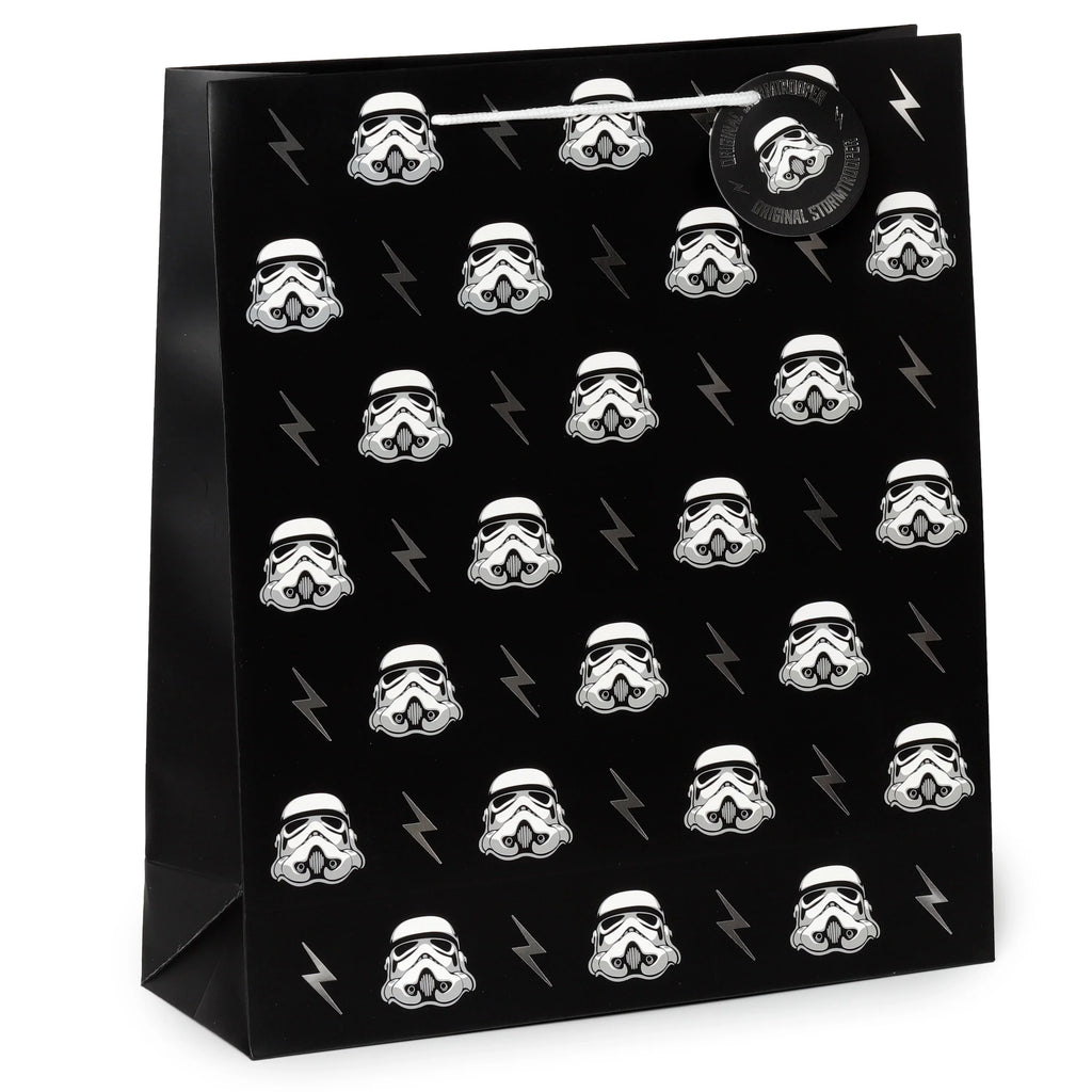Angled front view of an extra large black gift bag featuring a repeating pattern of white Stormtrooper helmets and grey lightning bolts, with white rope handles and a circular Stormtrooper tag.
