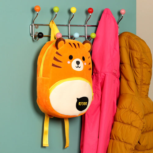 Front view of an orange plush tiger rucksack backpack hanging on a colorful coat rack.