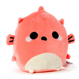 Coral pink pufferfish plush toy with large black eyes, white cheek details, a small black mouth, a cream belly, and striped side fins, shown from an angled front view.