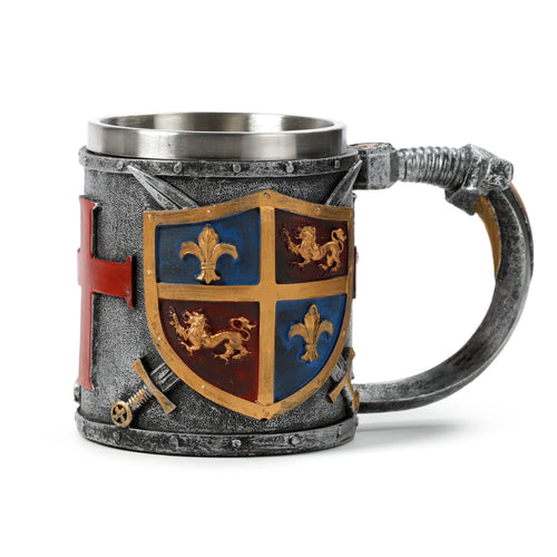 Angled view of a decorative tankard with a textured silver-grey finish, showcasing a central shield-shaped gold and silver coloured coat of arms featuring lion and fleur-de-lis designs. It also has an ornate handle and a red cross motif on its left side.