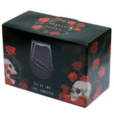Angled view of dark-coloured packaging for a set of Skeleton Hand glass tumblers, adorned with red rose and skull illustrations, and displaying a black tumbler with a skeletal hand design.