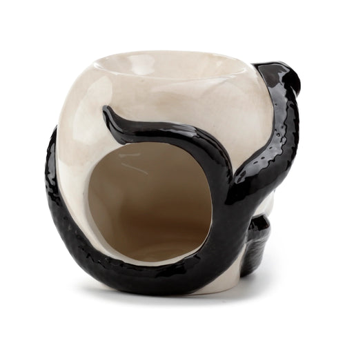 Angled view of a ceramic oil burner shaped like a light beige skull with a glossy black coiled snake design wrapping around it, showing the top oil bowl and side opening.