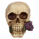 Front view of a bone-coloured Gothic skull ornament with dark eye sockets and textured cracks, adorned with a purple rose and green leaves on its right.