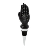 Front view of a novelty bottle stopper featuring a black mantric hand with white tarot palmistry symbols and zodiac signs, set on a silver and black ribbed stopper base, on a white background.