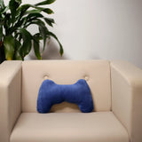 Lifestyle image showing a deep blue plush game controller cushion positioned centrally on a cream armchair, with a blurred green plant in the background.
