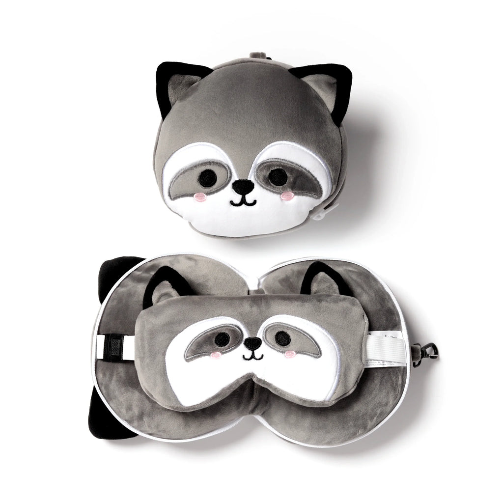 Overhead view of a grey raccoon plush travel pillow and eye mask set. One pillow is shown zipped as a round raccoon head, and the other unzipped to form a U-shaped neck pillow with a matching raccoon eye mask inside.