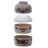 Exploded view of a grey round stacked bento lunch box, showing its four disassembled components. The top lid features Pusheen's eyes and ears, followed by a white translucent inner tray, then a compartment with Pusheen's full face, and a bottom compartment with Pusheen riding a scooter.