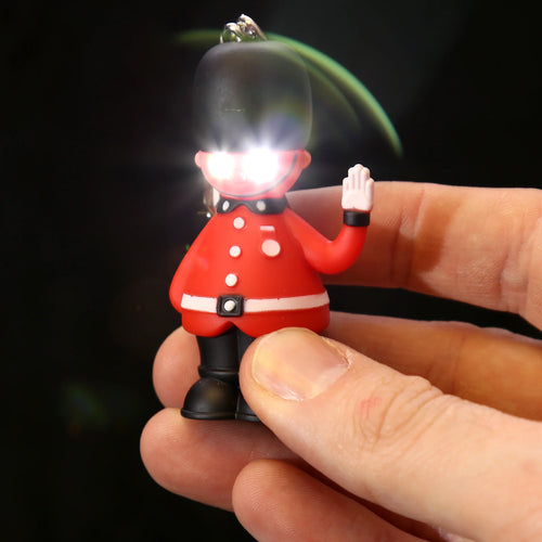 Close-up of a red and black British Guardsman LED keyring, featuring bright white lights glowing from its eyes, held in a person's hand.