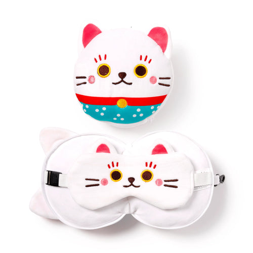 Overhead view of a white plush Maneki Neko lucky cat travel pillow and eye mask set. The travel pillow is shown both compact as a round cat head with a red and turquoise collar, and unfolded as a U-shaped pillow with an adjustable strap. The matching eye mask rests on the unfolded pillow; both items feature embroidered cat faces with pink ears.