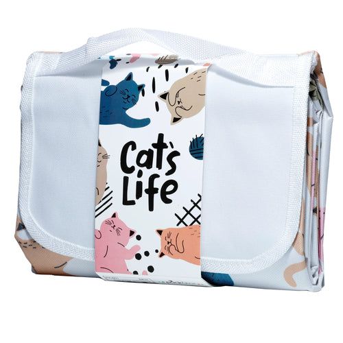 Front view of a folded 'Cat's Life' picnic blanket, secured by a white integrated strap that also forms a carry handle. A prominent label on the front displays Cat's Life text alongside colourful illustrations of cartoon cats in blue, beige, pink, and orange.