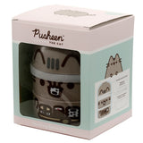 Angled front-right view of a Pusheen the Cat stacked bento lunch box in its light pink retail packaging. The clear window reveals the beige three-tiered lunch box, decorated with Pusheen's distinctive features on each level. The box top shows a lying Pusheen illustration, while the side panel provides details of the lunch box's compartments.