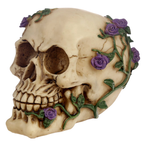 Angled view of a beige gothic skull decoration, intricately detailed with purple roses and green vines wrapping around its top and left side.