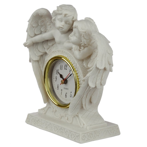 Angled view of an off-white mantle clock, depicting two winged cherubs with detailed faces, one looking forward and the other leaning towards the gold-rimmed white clock face with black numerals, set on an ornate, scroll-patterned base.