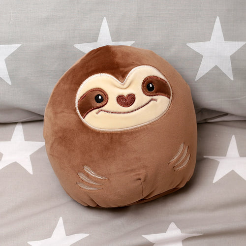 Angled view of a brown plush sloth cushion, featuring an embroidered light beige face with black eyes, heart nose, and smile, plus claw details on its sides. It rests on grey fabric with white stars.