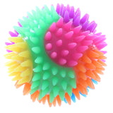 Front view of a vibrant rainbow-colored spiky bouncy ball, isolated on a white background.