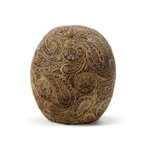 Angled view of a light-coloured damask skull ornament, featuring intricate swirling patterns.