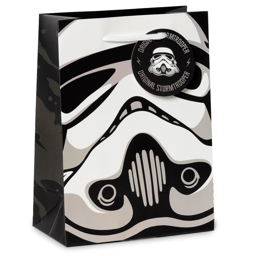 Front angled view of a medium gift bag featuring a black, white, and grey Stormtrooper helmet graphic. The bag has white rope handles and a matching round black tag with a helmet image.