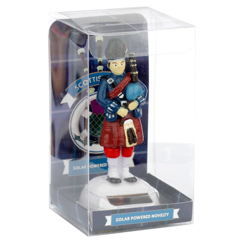 Front view of a Novelty Scottish Piper Solar Powered Pal figurine, in clear packaging, with kilt, bagpipes, and solar panel base.