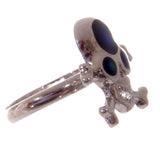 Angled view of a silver-coloured skull and crossbones mood ring, featuring iridescent black eye sockets and nose.