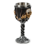 Angled view of a decorative goblet with a brushed metallic inner cup. The goblet's body is dark, designed with a caged appearance, from which bone-coloured skulls and skeleton hands emerge. Its twisted stem and circular base are intricately detailed with silver chains and additional skulls, all in a silver and black colour scheme.