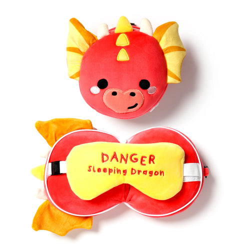 Overhead view of a red dragon travel pillow and matching eye mask set on a white background. The plush pillow shows a cartoon dragon's face with yellow horns and striped wings. The red eye mask features a yellow panel embroidered with 'DANGER Sleeping Dragon'.