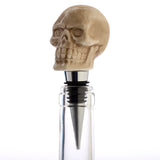 Angled view of a detailed bone-coloured ceramic skull bottle stopper, partially inserted into a clear bottle.