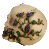 Angled view of a cream-coloured Gothic skull decoration, featuring sculpted purple roses and green vines, with visible left eye socket and jaw detail.