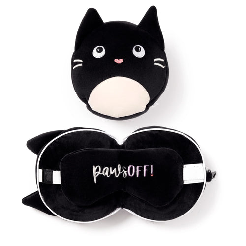 Overhead view of a black plush cat travel pillow, shaped like a round cat's face with embroidered white eyes, a pink nose, and a cream belly patch. Also visible is a matching black U-shaped neck pillow with cat ears, unzipped to reveal a black eye mask featuring 'paws OFF!' embroidered text in white and pink.