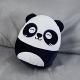 Angled white and dark blue panda plush toy, showing its embroidered smiling face with eyes, nose, and pink cheek blush on a soft grey background.