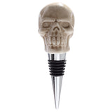 Front view of a novelty ceramic skull bottle stopper, featuring a detailed light beige skull atop a silver-coloured metal base with black rubber seals.