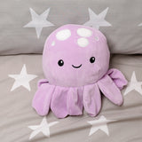Plush purple octopus cushion with white spots and a smiling face, displayed on a grey star-patterned fabric.