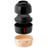 Exploded view of a round, stacked bento lunch box with its black components separated: a top lid, a middle tiered section, and a main container featuring a red exclamation mark. The bottom section is a beige container decorated with a London Guardsman's face and yellow striped patterns.