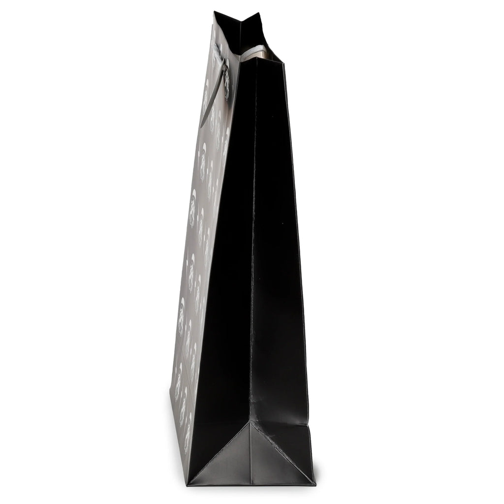 Angled view of an extra large black gift bag with white Stormtrooper helmet patterns and white rope handles.