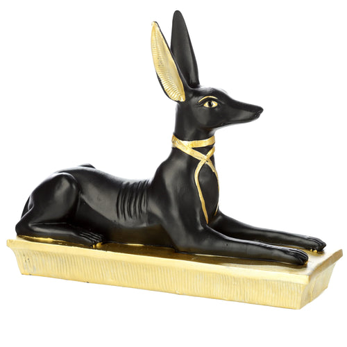 Side view of a decorative black and gold Egyptian Anubis jackal figurine reclining on a gold base, featuring golden ears, eyes, and an ornate collar.