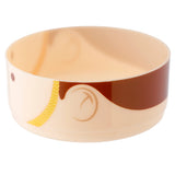 Angled view of a round, light beige lunch box tier. It features a dark brown band and a yellow, textured braid-like pattern on its side, along with subtle abstract brown curves.