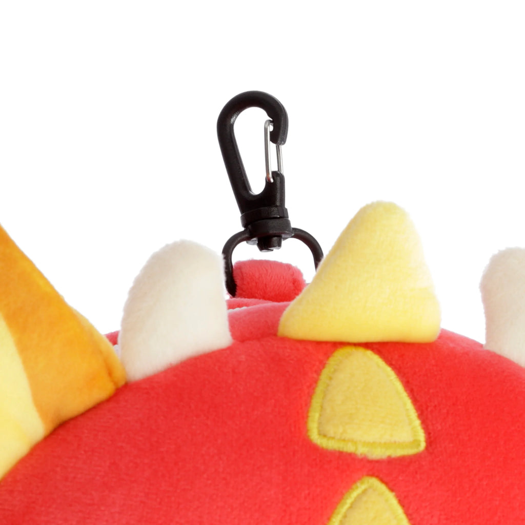 Close-up of the top of a compact red plush dragon travel pillow, featuring yellow and white horn-like details and a black carabiner clip.
