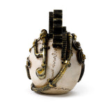 Steampunk skull ornament with dark cogs, golden pipes, and springs, shown in a rear view on a cream-coloured surface.
